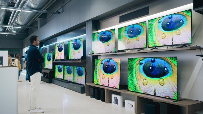 一个时尚男人的肖像，看着各种现代智能电视，高质量的分辨率显示和生动的色彩传输。客户在家电商店选购电视