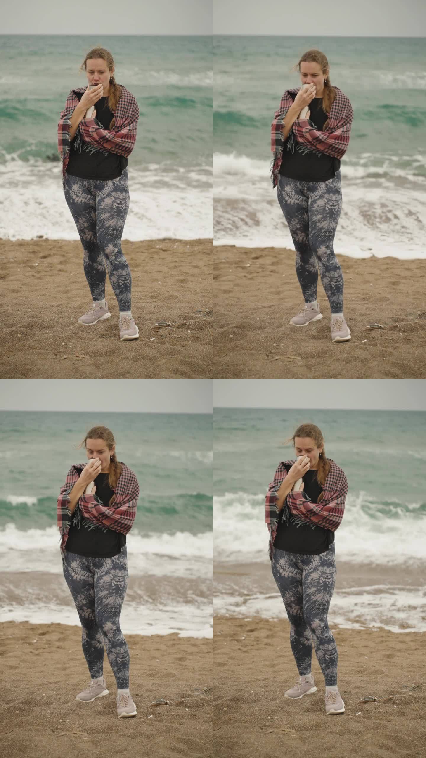 一位身穿格子衣服的年轻女子，在海浪的背景下用保温瓶喝茶。慢动作垂直视频社交媒体