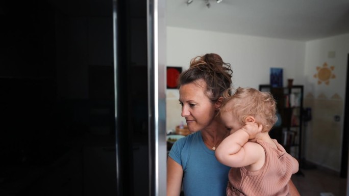 抱着孩子的妇女打开厨房的冰箱