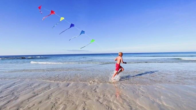 男孩在沙滩上奔跑，脚在水里，暑假的乐趣