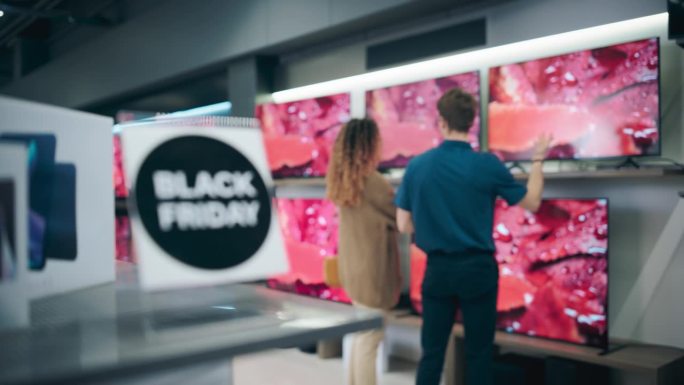 现代零售电子商店在黑色星期五销售活动。想买一台智能平板电视的女性。顾客探索折扣电视，由细心的销售团队