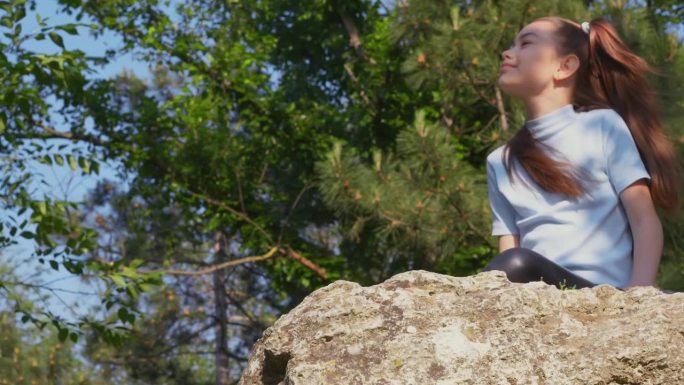 小女孩坐在森林里的一块岩石上，望着天空，做着梦