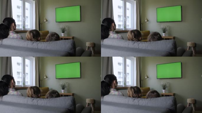 一家人坐在客厅的沙发上看电视。家庭和孩子坐在客厅沙发上的后视图，白天一起看绿色屏幕电视。