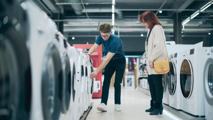 高级女顾客在挑选洗衣机时与家电商店店员接触。寻求高品质家电的中年妇女。顾客评价现代洗衣解决方案