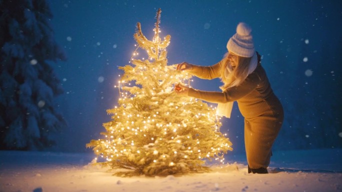 一名妇女在白雪覆盖的林间空地上装饰圣诞树