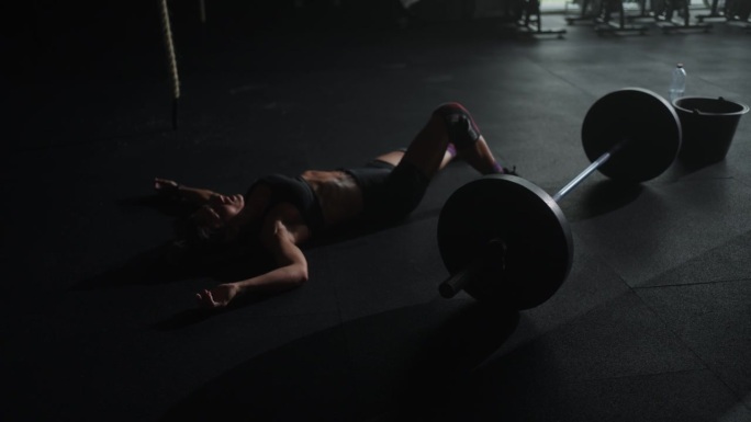筋疲力尽的女运动员躺在健身房杠铃旁边的地板上，锻炼后休息和呼吸困难