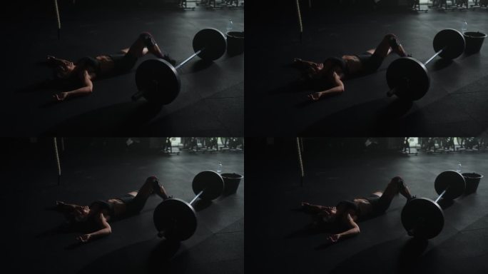 筋疲力尽的女运动员躺在健身房杠铃旁边的地板上，锻炼后休息和呼吸困难