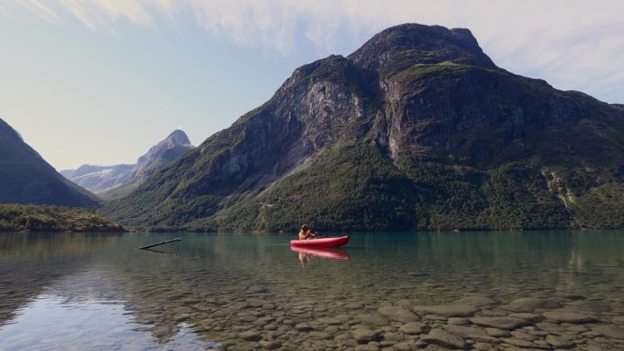 人们在一个原始的湖泊上划独木舟，穿过山脉，木筏漂浮在水面上