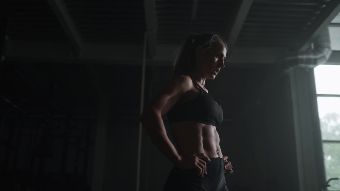 迷人的健美女性在健身房的肖像，肌肉发达的身体在黑暗的健身大厅的剪影