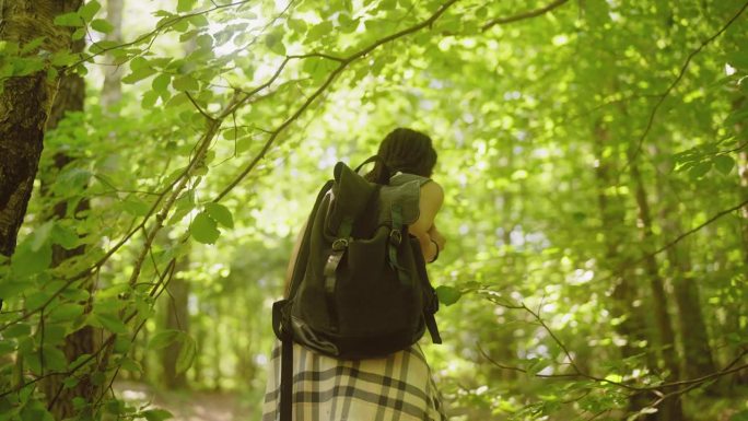 年轻女子走在森林的小路上，肩上背着背包