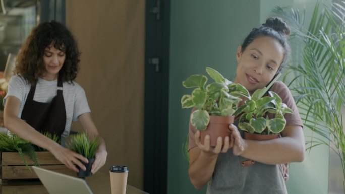 年轻的中东妇女在花店拿着盆栽植物，用手机接客户的订单