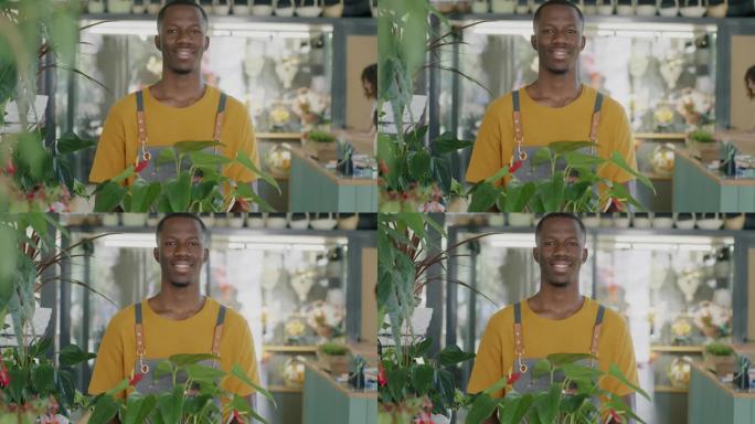 男性花商的肖像，非洲裔美国人站在花店拿着绿色植物，微笑地看着镜头
