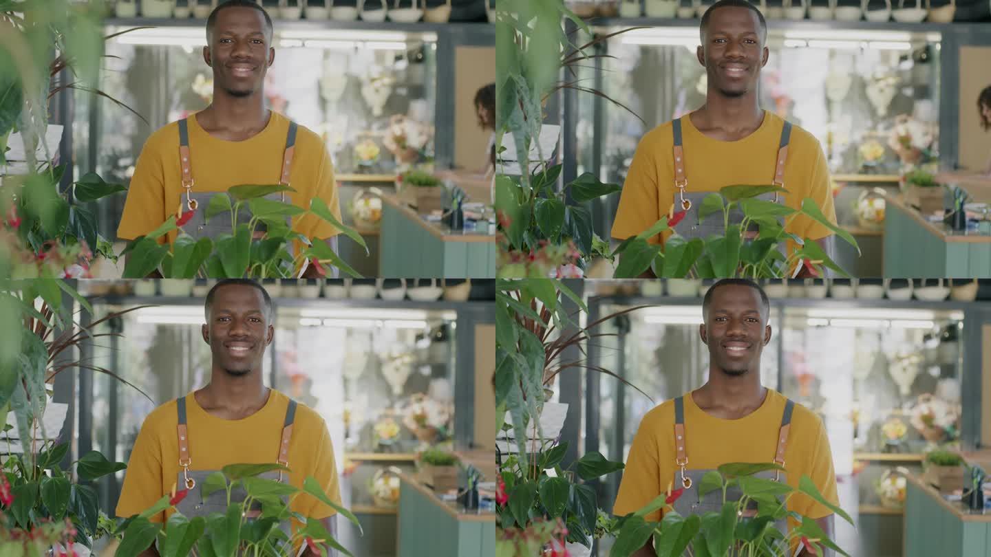 男性花商的肖像，非洲裔美国人站在花店拿着绿色植物，微笑地看着镜头