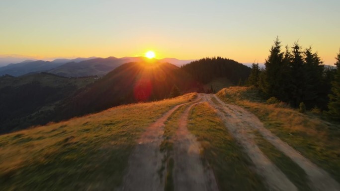 跨越山顶的越野路。黑暗的土路被明亮的夕阳照亮。在野生山林中令人惊叹的日落景色。美丽的自然景观