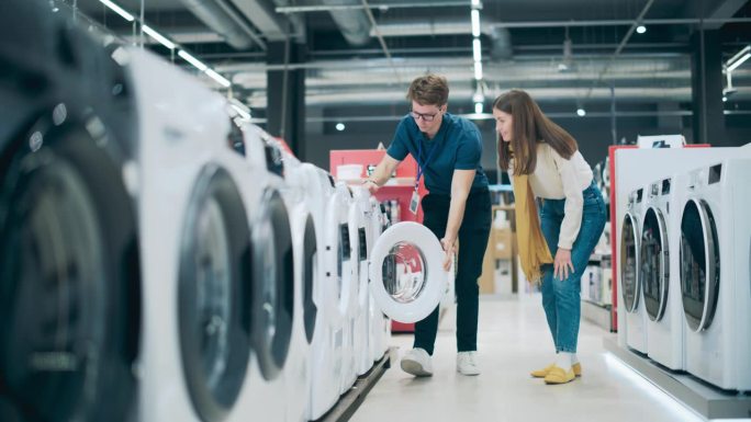 一位女顾客向家用电器零售专家寻求购买洗衣机的建议。年轻女子在百货公司探索当代洗衣设备的选择