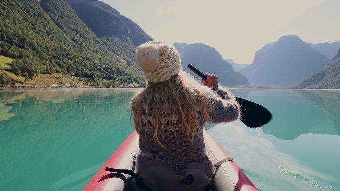 一个美丽的女人在一个原始的湖上划桨穿过山脉的后视图