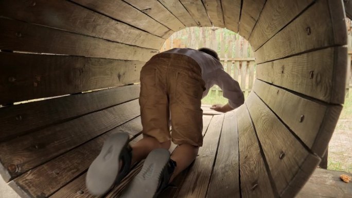 可爱的男孩在夏季冒险公园爬过木制的管道或隧道。孩子们在户外玩耍，孩子们玩得开心，暑假和假期