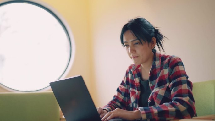 年轻的亚洲妇女在现代化的会议室里聚精会神地玩电脑。她为新项目与国际公司进行沟通。