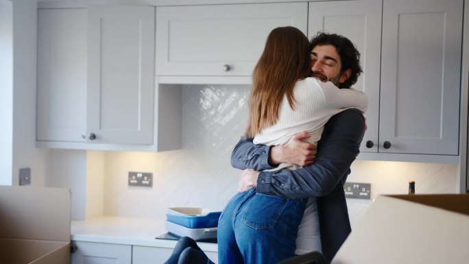 兴奋的夫妇在新家的厨房里庆祝拥抱，因为他们在搬家那天打开了箱子