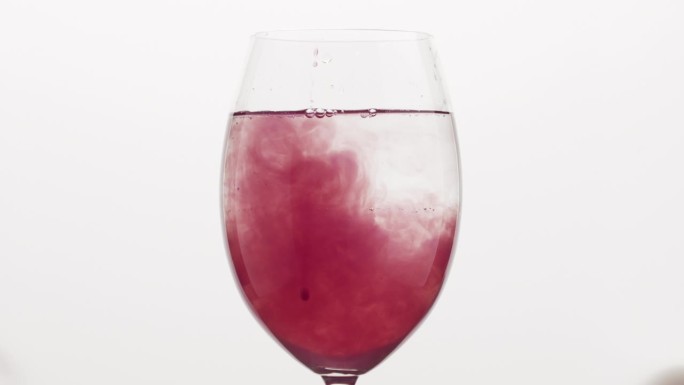 将蓝莓汁倒入酒杯中的水中