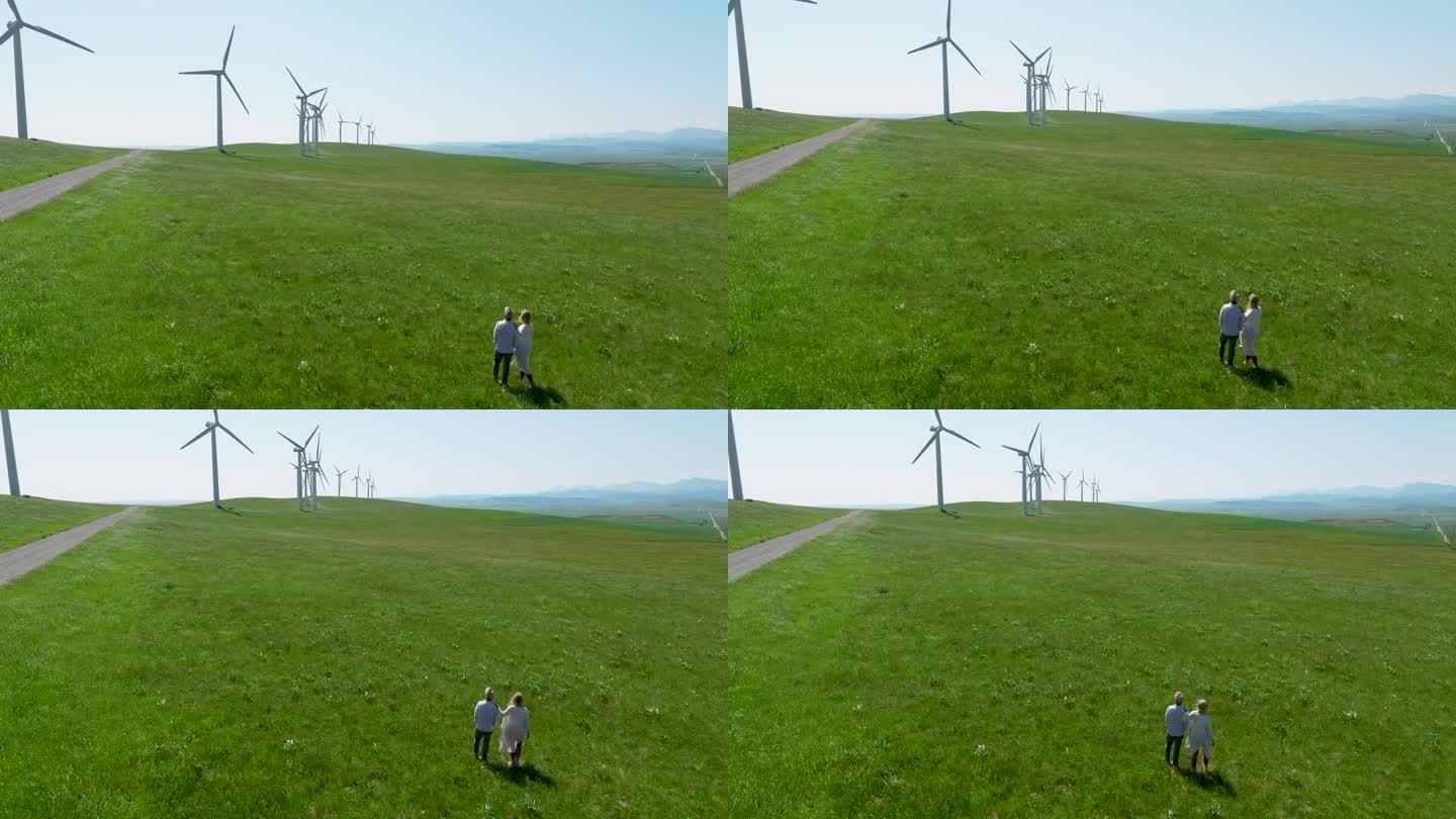 一对老年夫妇走进风力涡轮机下的草地