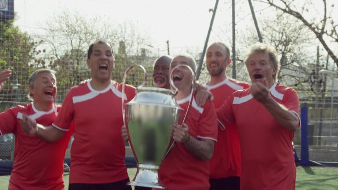 一群快乐的中年男性足球运动员边跳边喊边举起奖杯