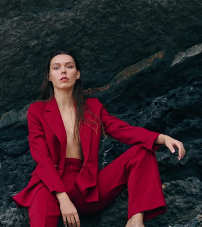 自信的女人穿着红色套装坐在山崖边。岩石垂直摆位模型