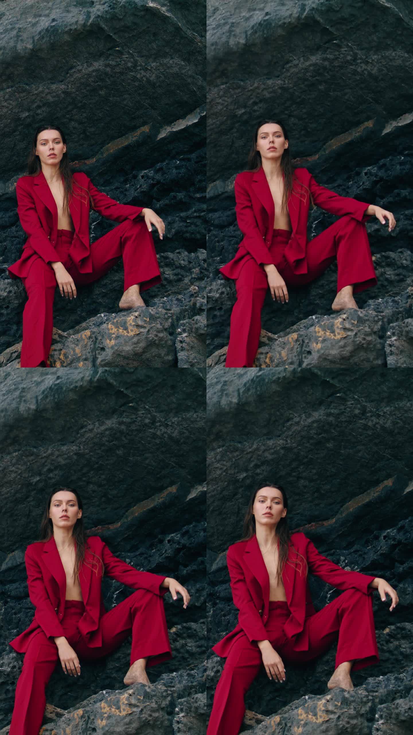自信的女人穿着红色套装坐在山崖边。岩石垂直摆位模型