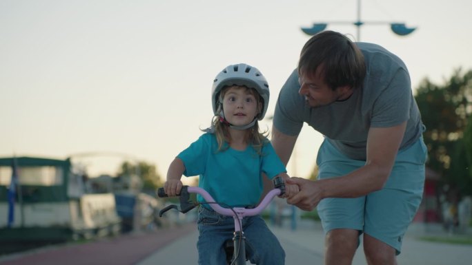 爸爸教女儿骑自行车。幸福家庭的童年梦想概念。爸爸和小女儿在公园里学骑自行车。幸福的家庭喜欢户外运动，