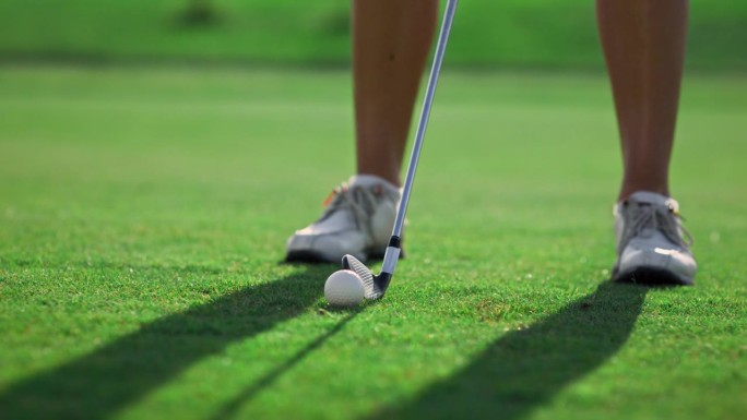 高尔夫球员的双腿站在高尔夫球场的草地上。女子在室外挥杆高尔夫球