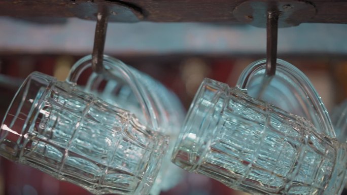 老式的玻璃马克杯挂在酒吧柜台上方的架子上