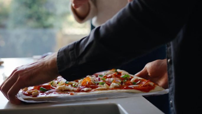 一对夫妇在厨房里把自制的新鲜披萨放进烤箱的特写