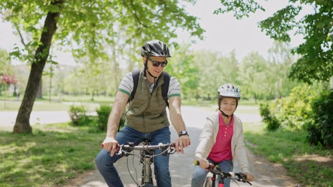 阳光明媚的一天，父亲和女儿在公园里骑自行车