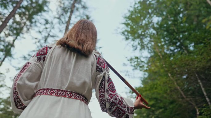 年轻女子演奏木管木笛-乌克兰特伦卡或泰林卡在森林背景。民间音乐概念。乐器。身穿传统刺绣衬衫的音乐家。