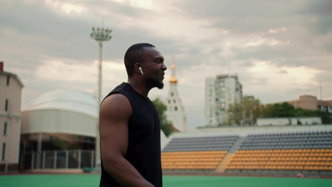 一名身穿黑色运动服的黑皮肤男子走过城市体育场，休息时回头望着灰色的天空