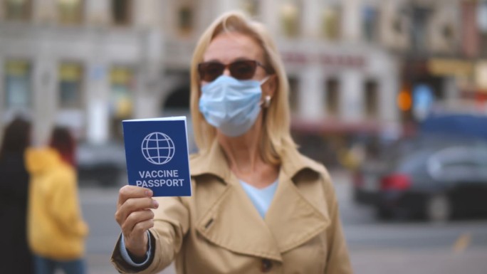 成年妇女的肖像，戴着口罩，在镜头前展示疫苗护照