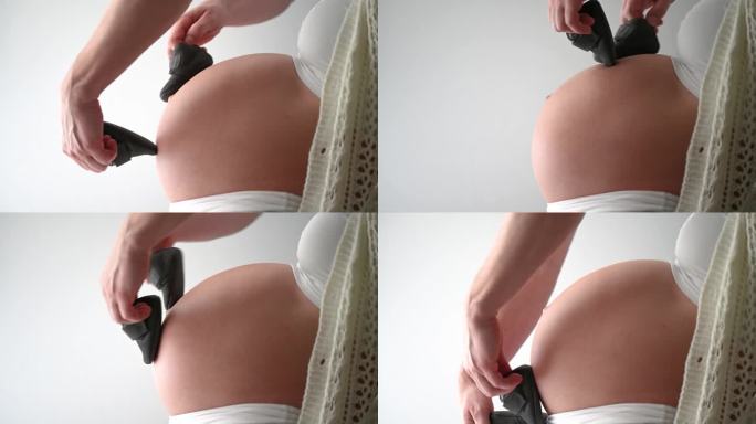 婴儿鞋在孕妇圆肚子上跳“月亮舞”的侧视图。妊娠晚期-第39周。侧视图。白色背景。自然光线。