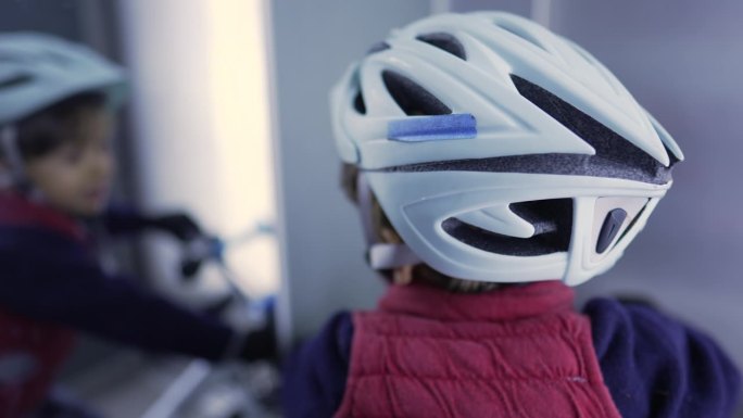 电梯内戴自行车头盔的儿童背部。小孩戴着自行车护具看着镜子里的倒影