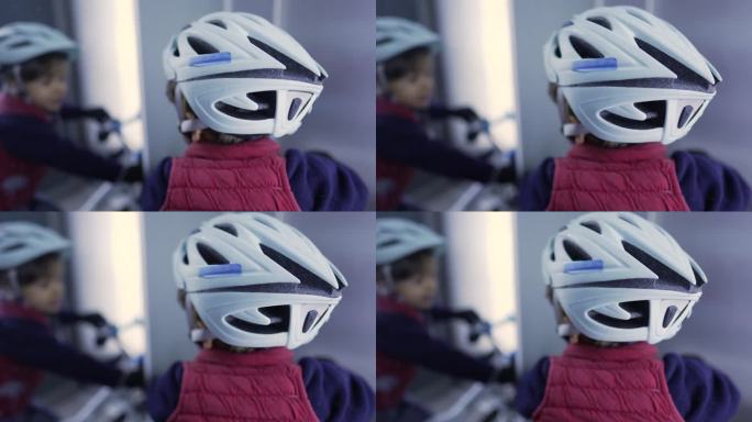 电梯内戴自行车头盔的儿童背部。小孩戴着自行车护具看着镜子里的倒影