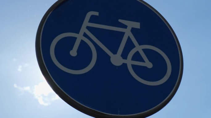 圆形道路标志，蓝色背景白色自行车，蓝色天空背景下的自行车专用道。自行车道杆上的蓝色圆形标志
