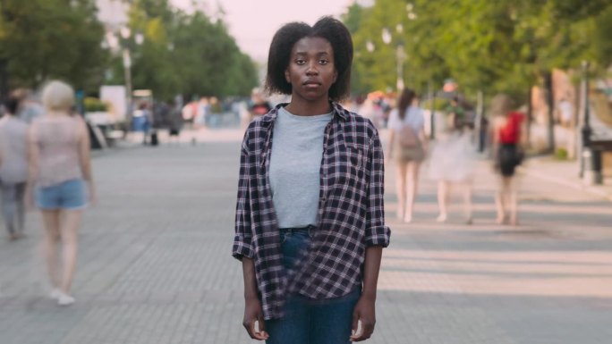 在模糊的城市背景下，孤独的非洲裔美国女士站在繁忙的步行街上的延时肖像