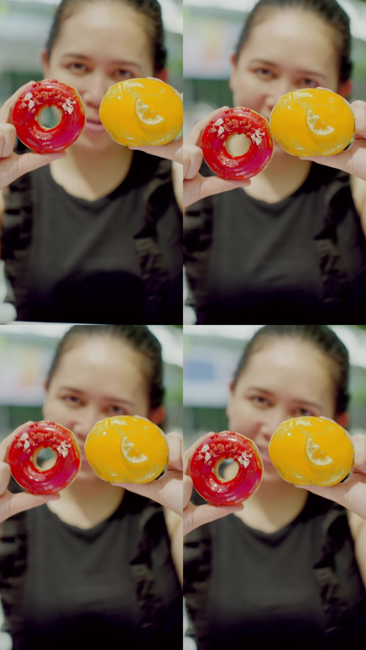 特写:看着镜头:亚洲中年妇女双手拿着两个红色和黄色的甜甜圈，一边玩一边移动甜甜圈，一边开心地跳舞