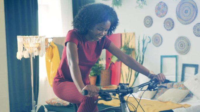 运动在家，健身在家的理念。一位开朗的非洲女士正在用一辆自行车在封闭室内训练