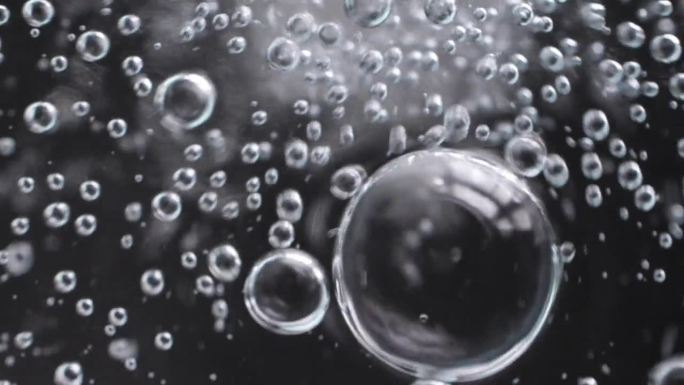 慢动作特写场景上的小气泡连接在一起成为一个更大的一个孤立的黑色背景，气泡质地的苏打水饮料时，气体释放