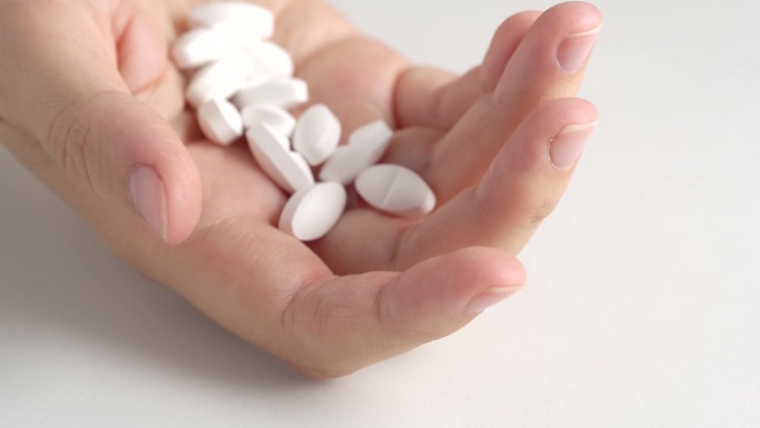 手里拿着一堆白色药片的女人，马克罗。一堆白色的大药丸，椭圆形，细长的形状从药瓶落入手掌。