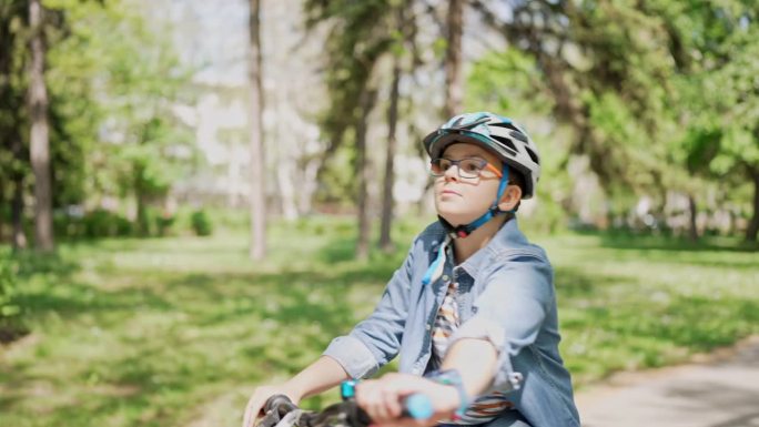 在阳光明媚的日子里，戴着护具的男孩在公园里骑自行车