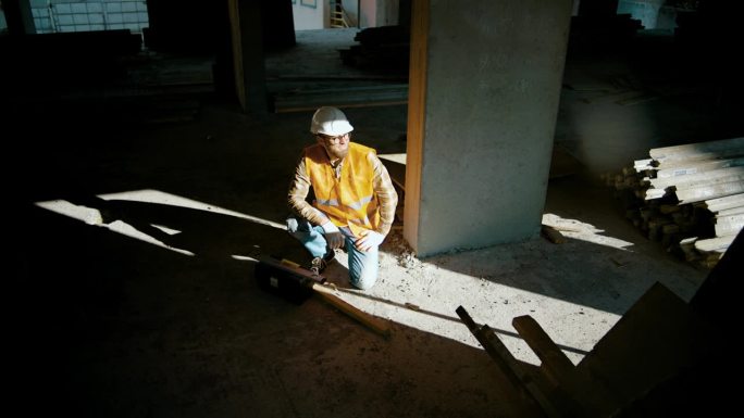 工地上，一名建筑工人坐在墙边，打开工具箱。人类的影子