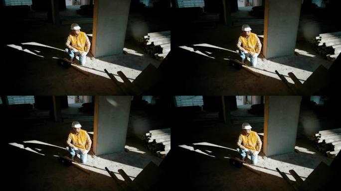 工地上，一名建筑工人坐在墙边，打开工具箱。人类的影子