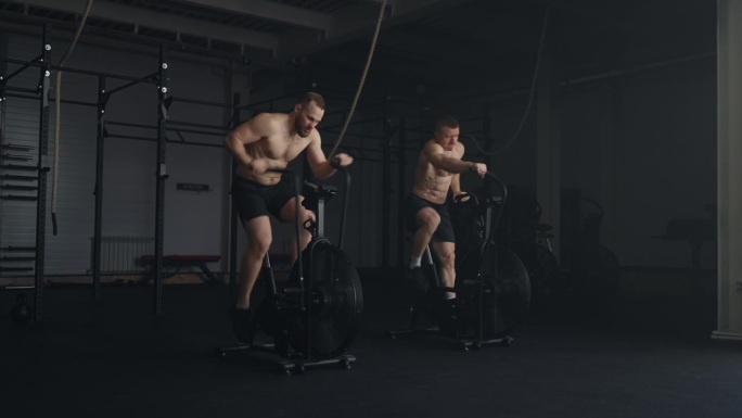 两个健硕的运动员在健身房的固定自行车上训练，高强度有氧运动，健康的生活方式
