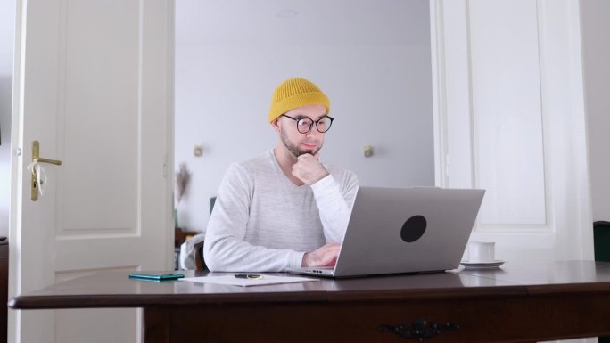 戴着眼镜、留着胡子的年轻白人男子正在用笔记本电脑写文件。远程工作，自由职业者和在线人力资源的概念